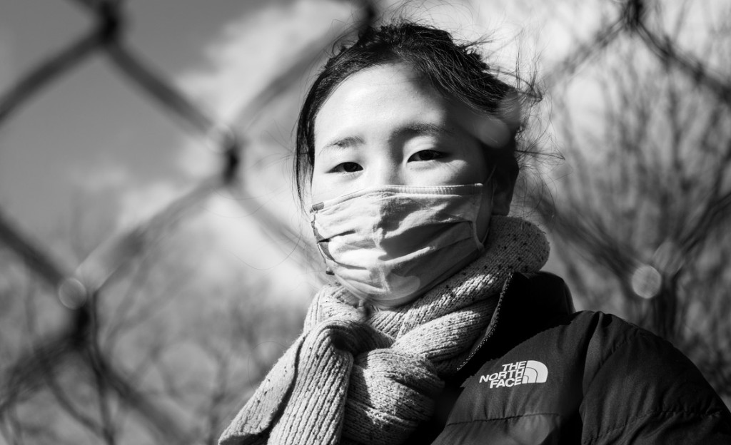 Portrait of a woman in a mask by a fence